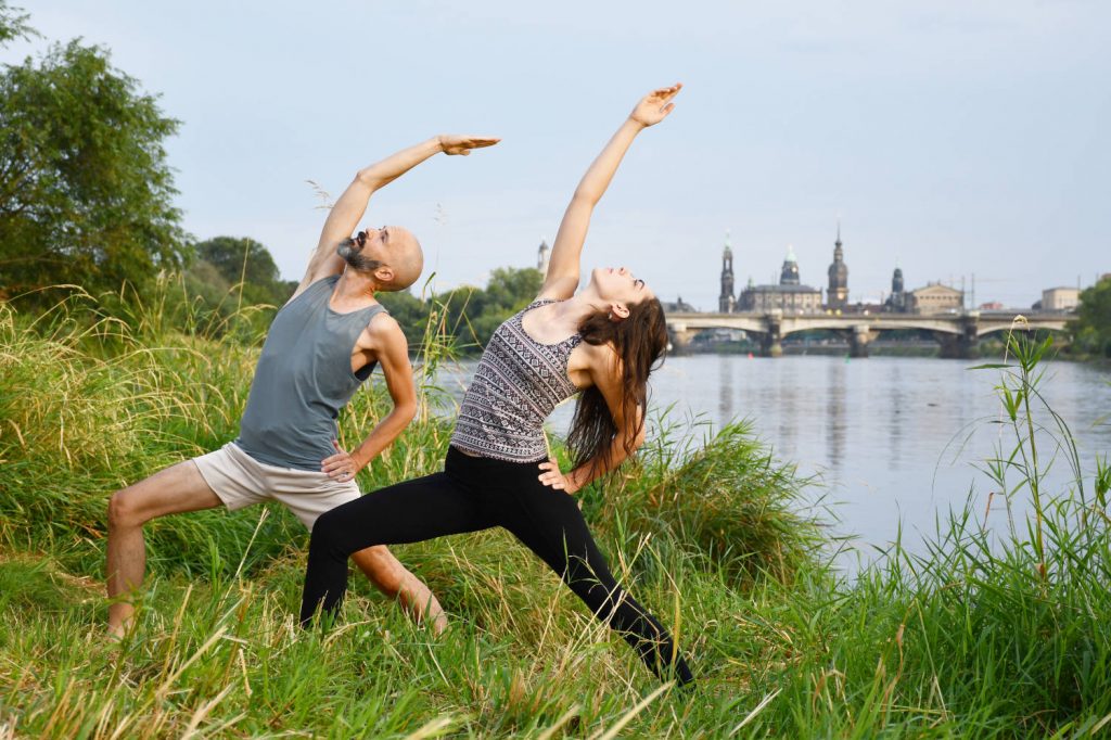 Matty unterrichtet eine Yoga-Teilnehmerin die friedlichen Kriegerhaltung an der Elbe in Dresden.