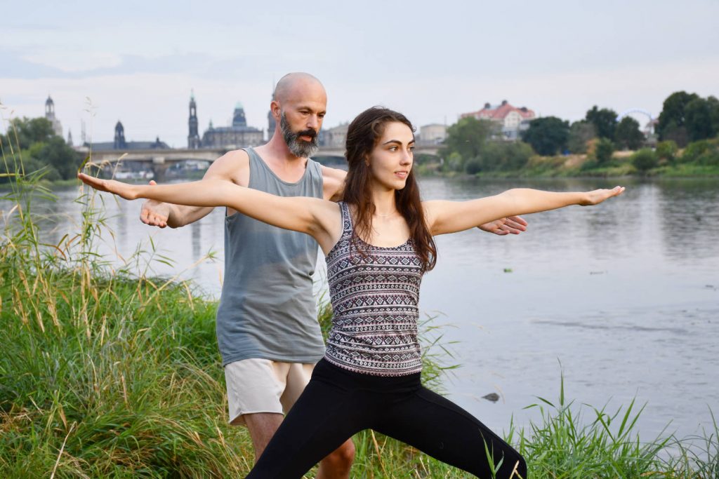 Matty unterrichtet eine Yoga-Teilnehmerin die Kriegerhaltung an der Elbe in Dresden.